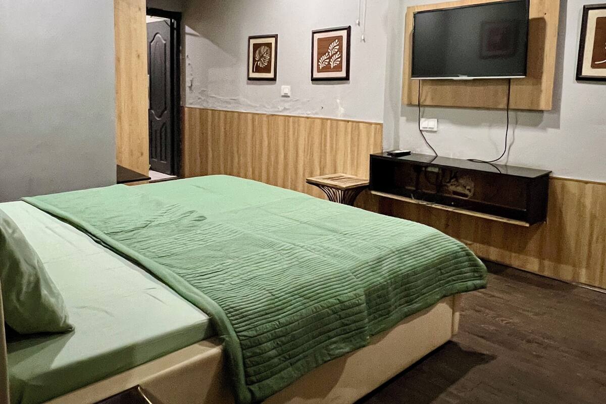 Ein Schlafzimmer mit einem Bett, einem an der Wand montierten Fernseher, einem Ventilator und gerahmten Bildern.