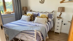 A bed with striped bedding, a bedside table with a lamp, and a small drawer unit.
