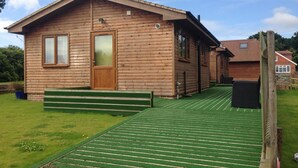 A wooden cabin with a green deck, a door, and windows.