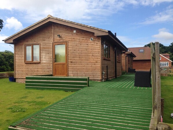 A wooden cabin with a green deck, a door, and windows. - Tranquil Countryside Lodge Retreat Near Rye & Coast (Hastings)