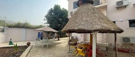 Un patio con una estructura de techo de paja, asientos al aire libre y un edificio al fondo.