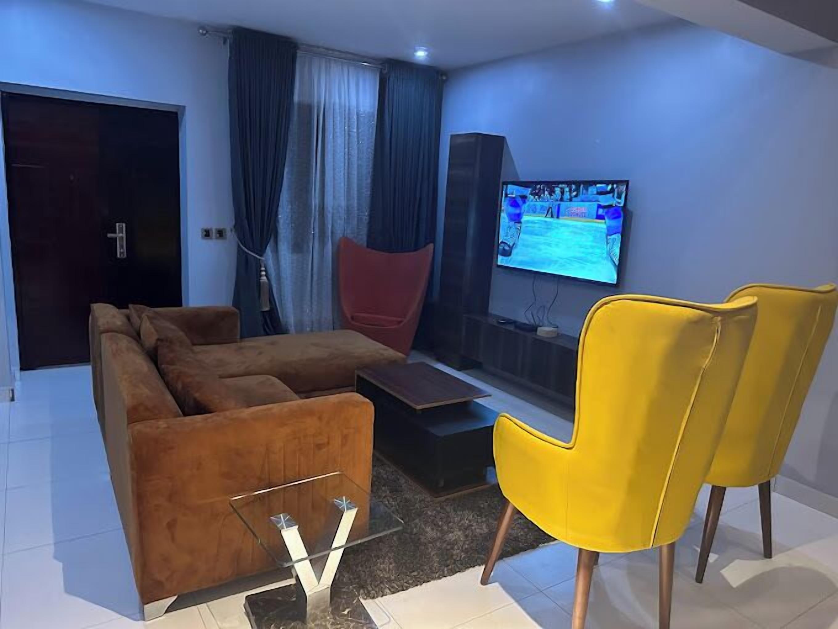 A modern living room with a sofa, a yellow armchair, a TV, and a glass coffee table.