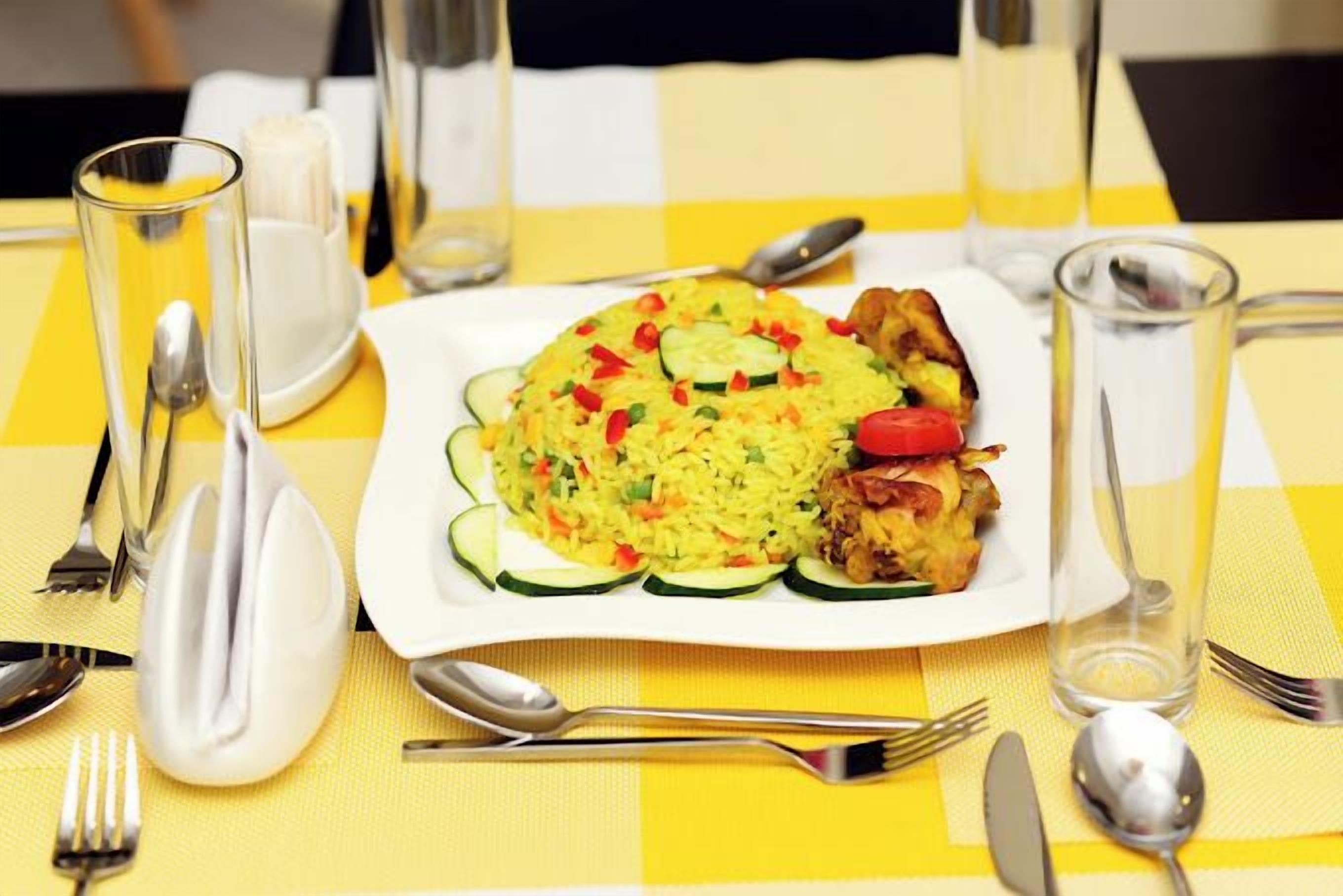 Una mesa servida con arroz amarillo, verduras y carne, acompañada de cubiertos y vasos.