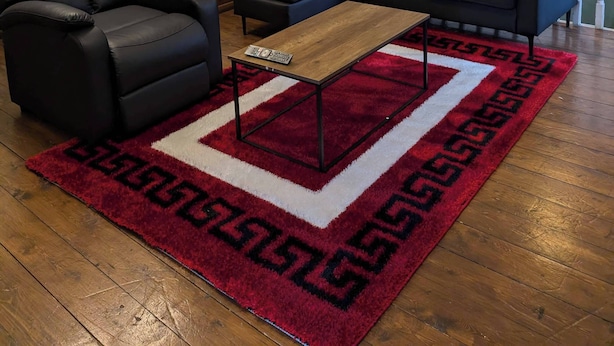 A living room with a black leather sofa, a black leather armchair, a wooden coffee table, and a red and white patterned rug. There is a staircase with a white railing and a black door in the background. - 3b-10min City Airport, Parking, No Parties Allowed (London)