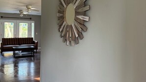 A spacious room with a large mirror on the wall, a ceiling fan, and a wooden floor.