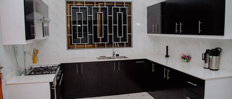 A modern kitchen with black and white cabinetry, a stainless steel sink, and a marble backsplash.
