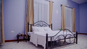 A neatly made bed with white linens in a room with patterned curtains and a marble floor.