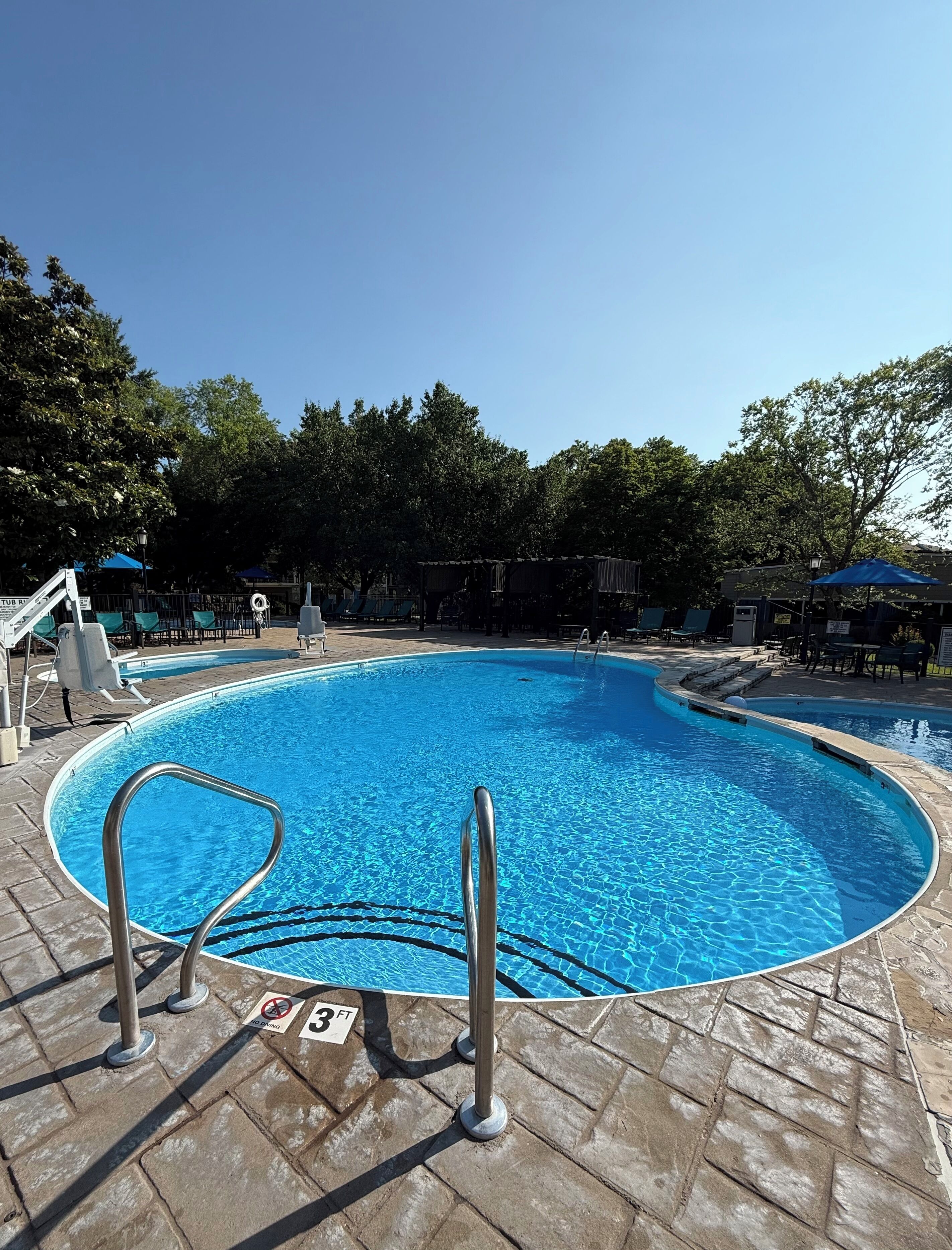 Una piscina con una escalera metálica, sillas de descanso y una zona de estar techada.