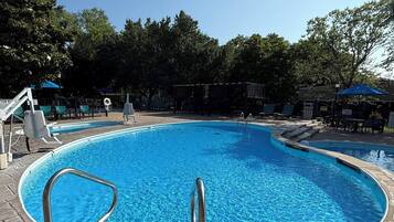 Una piscina con una escalera metálica, sillas de descanso y una zona de estar techada.