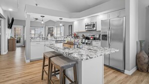 A modern kitchen with white cabinetry, a large island with bar stools, stainless steel appliances, and a wooden floor. - 3 King Suites near Silver Dollar City & the Strip (Branson)