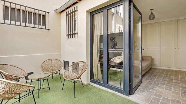 Un pati amb cadires de vimetla i una porta de vidre que dona a una habitació amb sofà i armaris.
