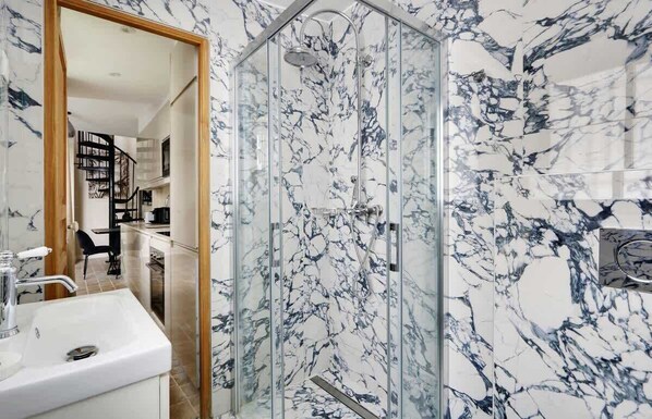 A bathroom with a glass-enclosed shower, a sink, and marble-patterned walls.