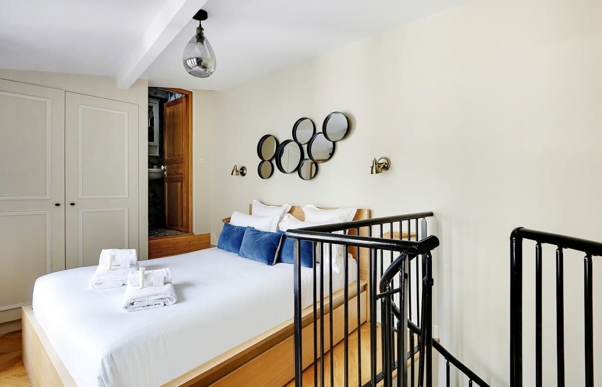 Ein Schlafzimmer mit einem Bett, einer Holztür, einem an der Wand befestigten Spiegel und einer Treppe.