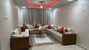 Un salon moderne avec un canapé d’angle, une table basse ronde et un luminaire suspendu au plafond.