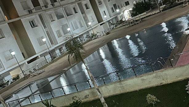 Un immeuble de grande hauteur doté de nombreux balcons, d’un élément décoratif aquatique réfléchissant et d’une pelouse bien entretenue.