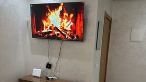 Une pièce dans laquelle un téléviseur à écran plat est fixé au mur et diffuse une image de feu. En dessous du téléviseur, on trouve un meuble de rangement en bois sur lequel est posé un appareil blanc.