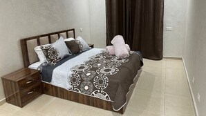 Une chambre à coucher comprenant un lit, une table de chevet, une commode et une grande fenêtre avec des rideaux.