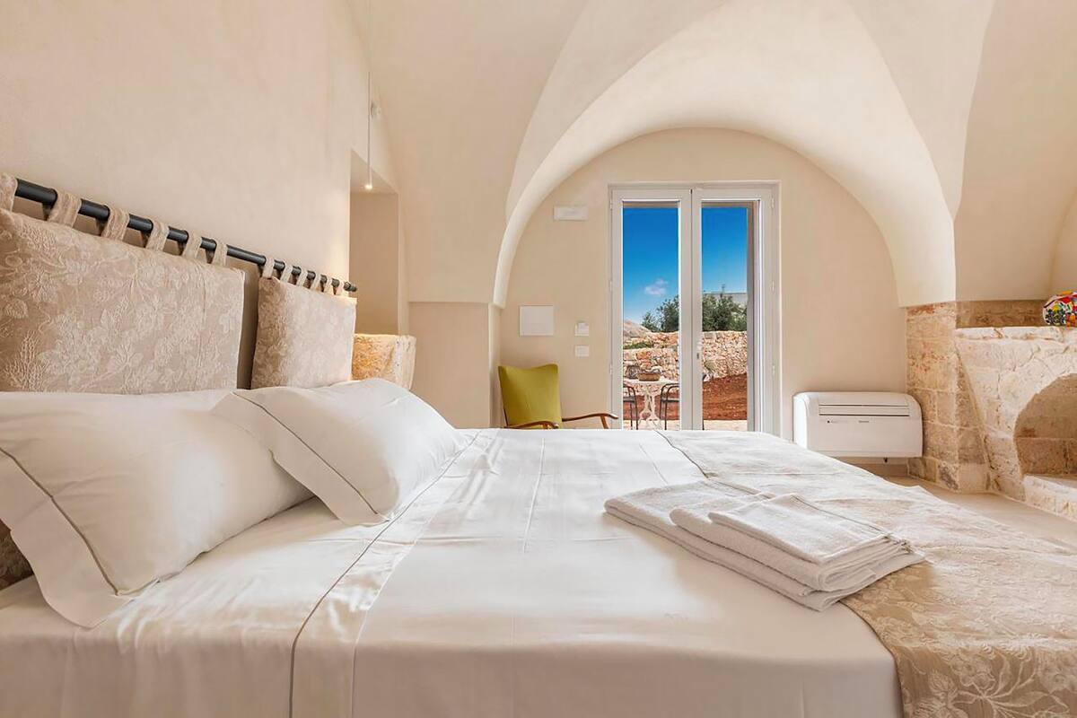 Una habitación de hotel con una cama grande, vistas a través de un arco y una chimenea de piedra.