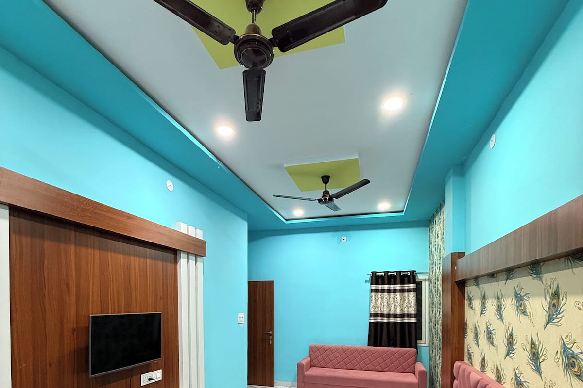 Une chambre moderne avec un lit, une télévision, un ventilateur de plafond et une fenêtre avec des rideaux.
