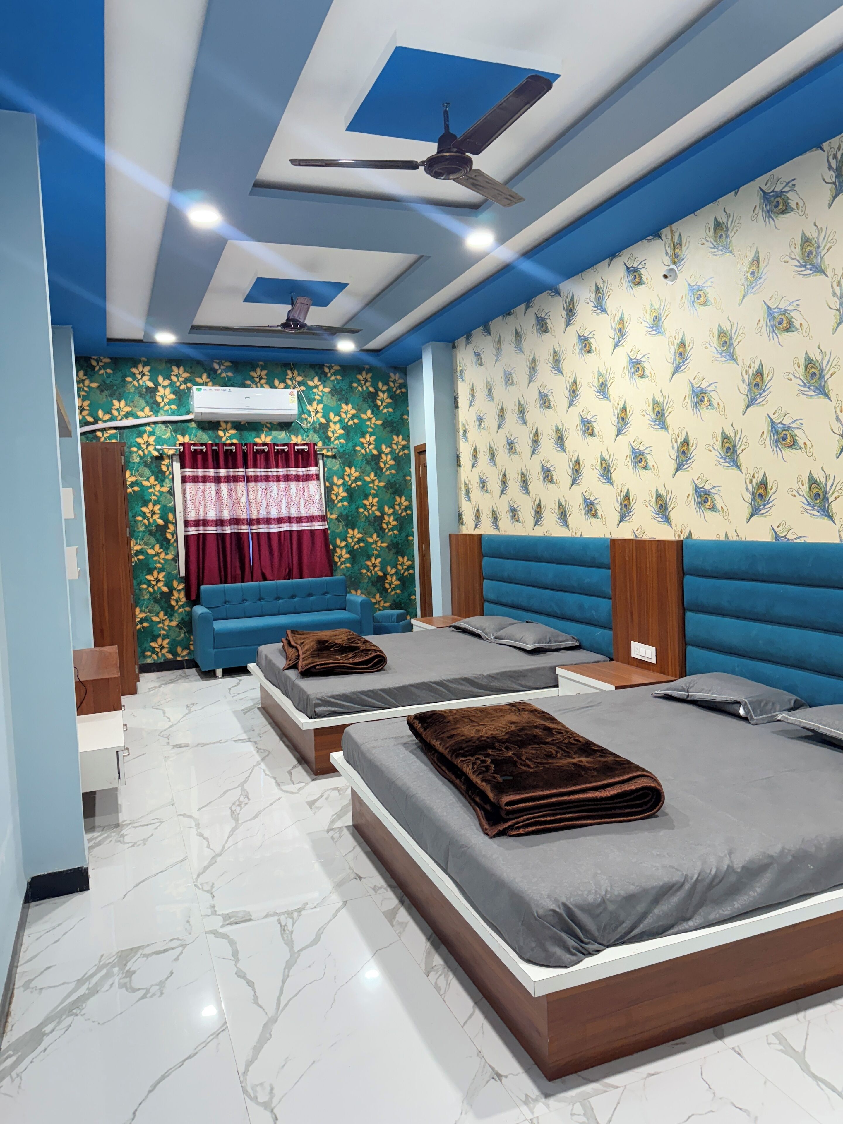 A bedroom with two beds, a blue sofa, a red curtain, and a ceiling fan.