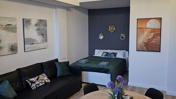 Cozy living space with a sofa, dining table, and bed, surrounded by artwork and a chandelier.