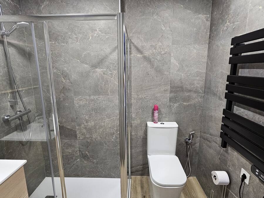 A modern bathroom with a glass-enclosed shower, a white toilet, and a wooden vanity.