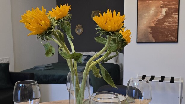 A dining table set with plates, glasses, and a vase with sunflowers. - Inspiracion Valencia (València)