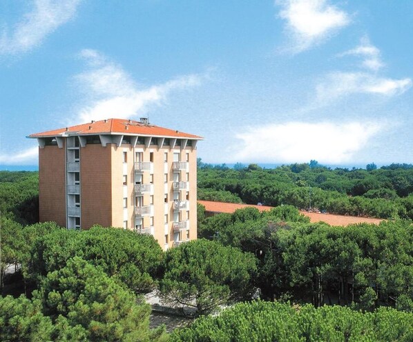 Un edificio de varios pisos con balcones, rodeado de abundante vegetación y un cielo despejado.