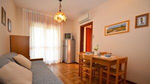 Ein gemütliches Zimmer mit einer Couch, einem Esstisch mit Stühlen, einem Fernseher und einer Klimaanlage.
