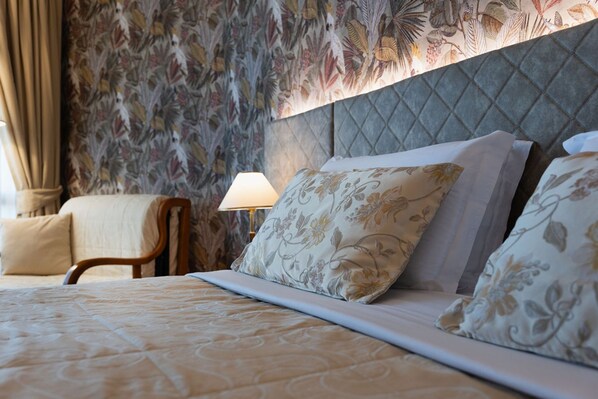 A neatly made bed with floral-patterned pillows and a quilted headboard. - Savoy Beach Hotel & Thermal SPA - Comfort Bedroom (Bibione)