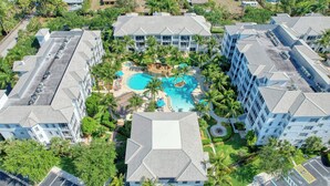 An aerial view of a resort with multiple buildings, a central swimming pool surrounded by palm trees, and a parking area. - Tropical Poolside Retreat! (Bonita Springs)