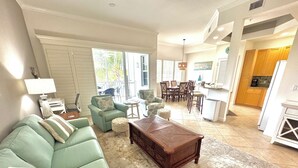 A living room with a green sofa, a wooden coffee table, and a dining area with chairs and a table. - Tropical Poolside Retreat! (Bonita Springs)