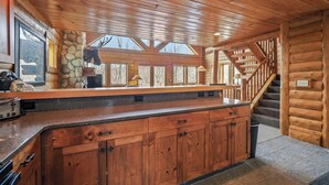 Interior de uma cabana de madeira com lareira de pedra, uma janela grande e uma escada.