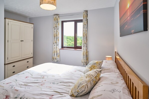 A bedroom with a bed, a wardrobe, a window with curtains, and a wall-mounted lamp. - Host Stay Coombe Cottage (South Molton)