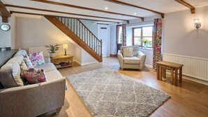 Un salon spacieux avec un escalier en bois, un ensemble de canapés, une table basse et un tapis.