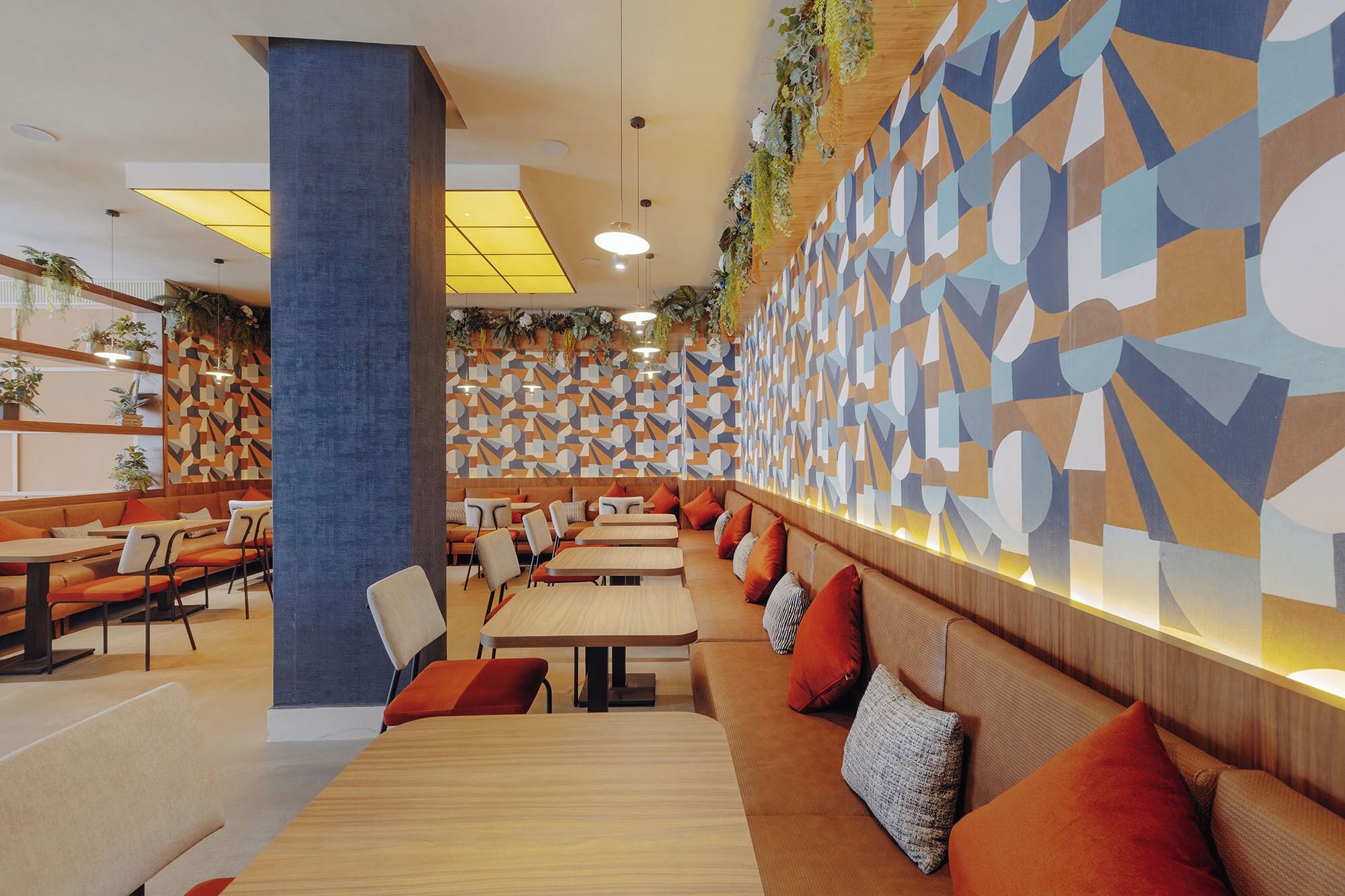 Un restaurant moderne avec des motifs géométriques sur les murs, des tables en bois et des sièges rembourrés de couleur orange.