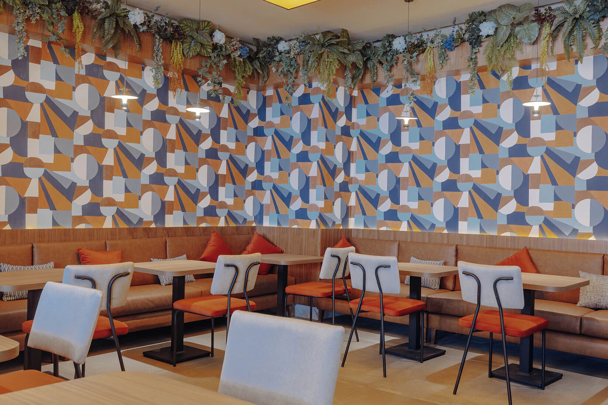 Interior moderno de restaurante con paredes de patrón geométrico, muebles de madera y plantas colgantes.
