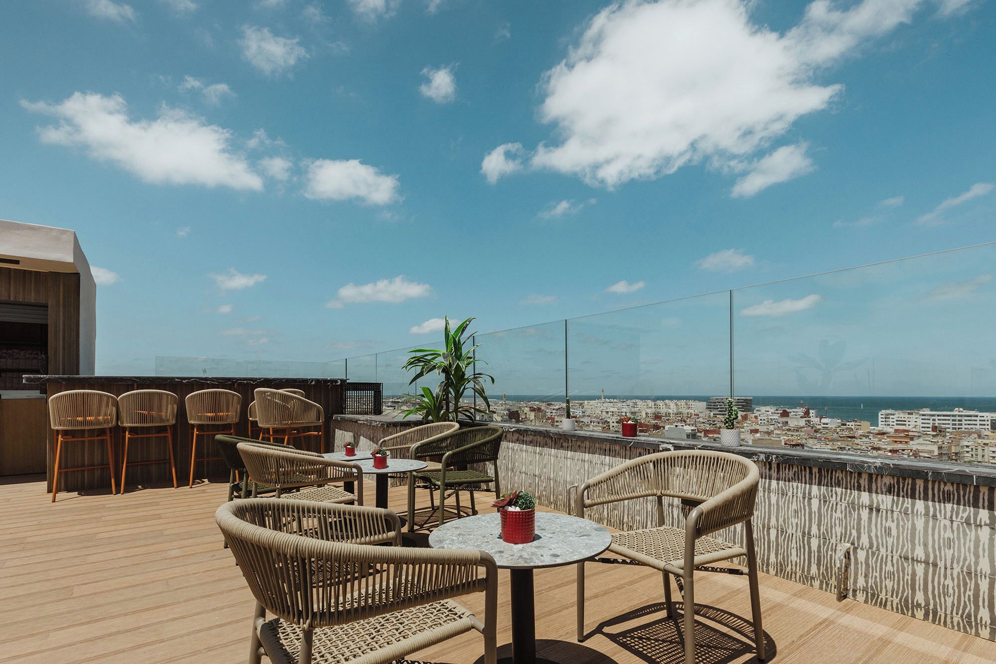 A rooftop terrace with wicker furniture, a small table, and potted plants.