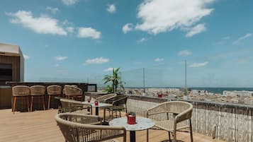Eine Dachterrasse mit Korbmöbeln, einem kleinen Tisch und Topfpflanzen.