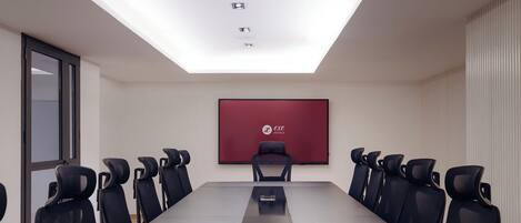 A conference room with a long table, black chairs, a red logo on the wall, and a skylight.