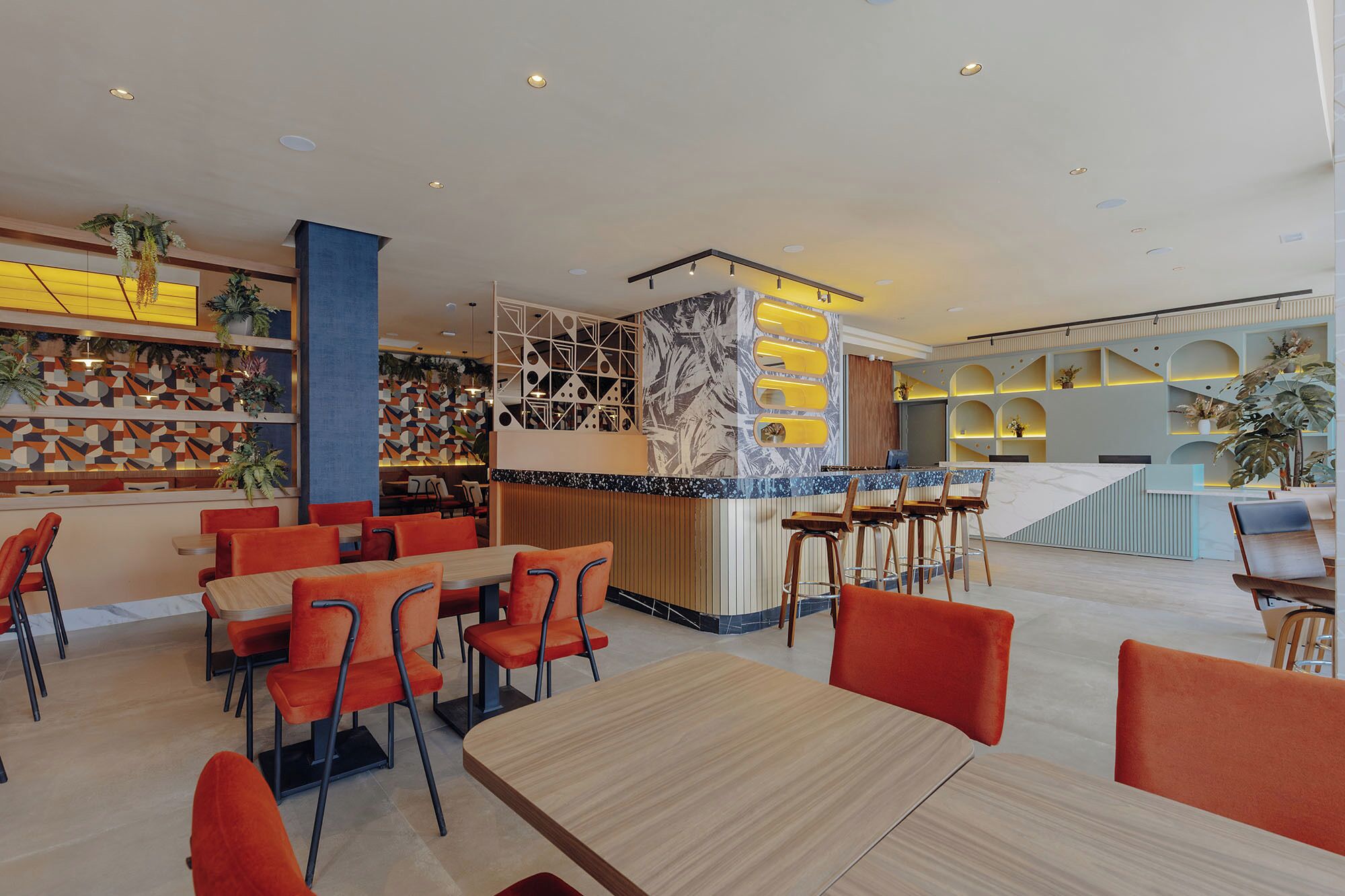 A modern restaurant with a bar area, multiple seating options including tables and bar stools, and a variety of plants and decorative elements.