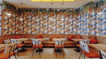 Interior de restaurante moderno com paredes com padrão geométrico, assentos laranja e plantas pendentes.