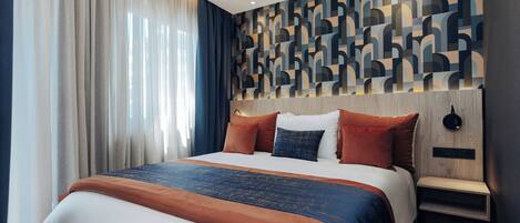 A modern hotel room with a large bed, a wooden headboard, and a geometric-patterned wall.