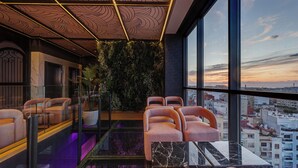 Un salón moderno con vistas a la ciudad, que cuenta con barandilla de vidrio, asientos cómodos y un techo decorativo.