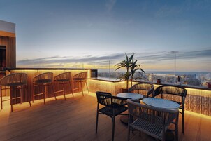 Una terraza en la azotea con piso de madera, una zona de bar con taburetes y una mesa con sillas.