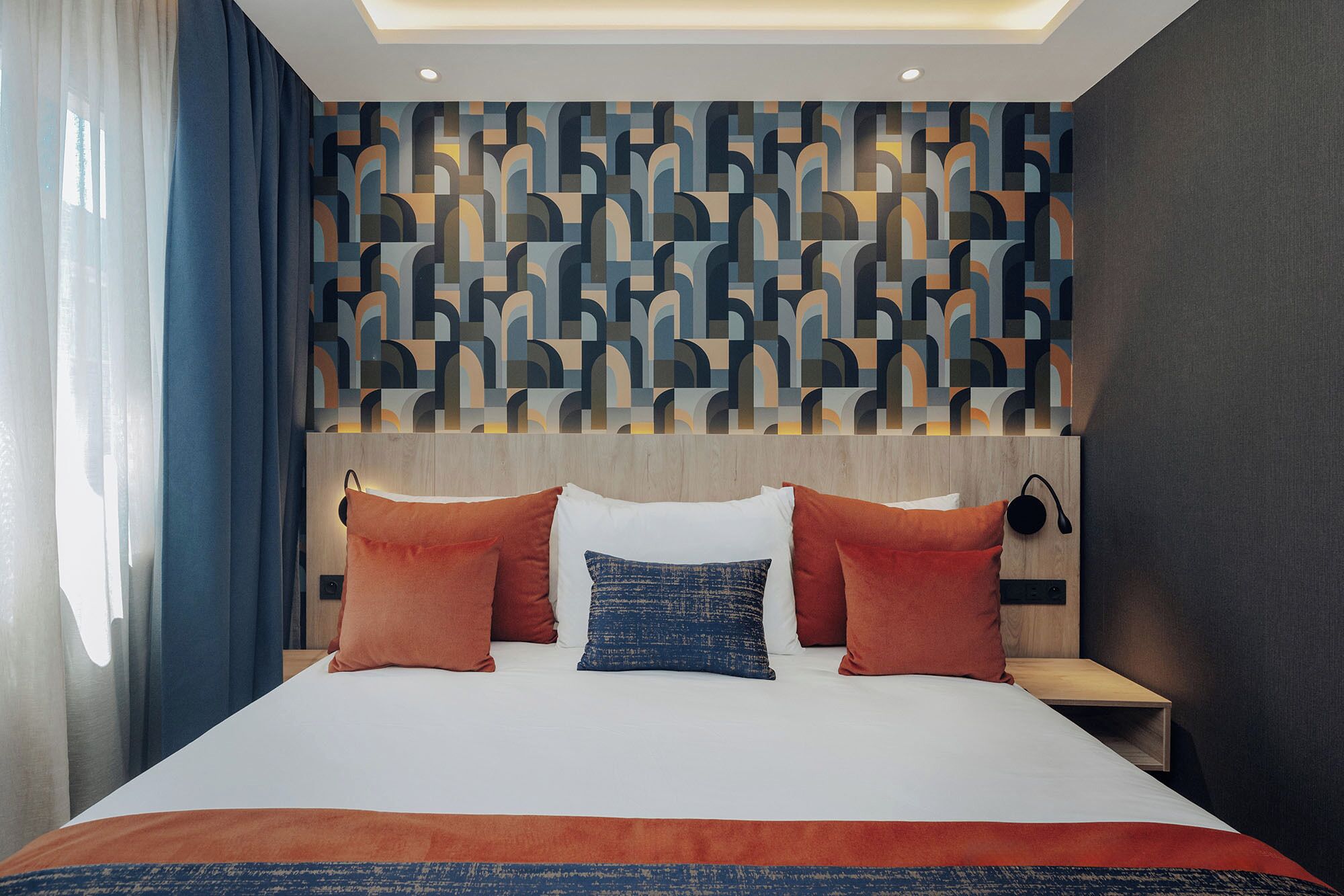 Una habitación de hotel moderna con una cama grande, un cabecero de estampado geométrico y una mesita de noche con lámpara.