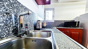 A kitchen with granite countertops, stainless steel sink, red cabinets, and a window providing natural light. - RESIDENCE FAMILIA PHOENIX (Douala)