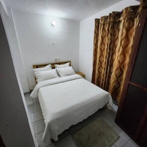 Een slaapkamer met een bed, nachtkastje, een wandlamp en een gordijn met patroon.