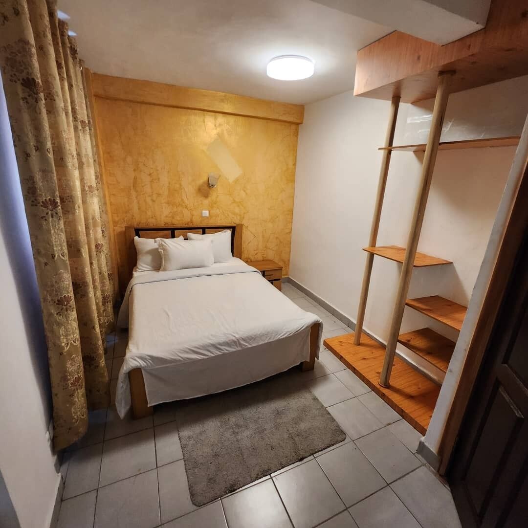 A bedroom with a bed, a nightstand, a wooden wardrobe, and a window with curtains.