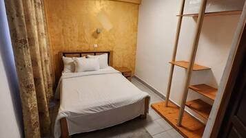 A bedroom with a bed, a nightstand, a wooden wardrobe, and a window with curtains.